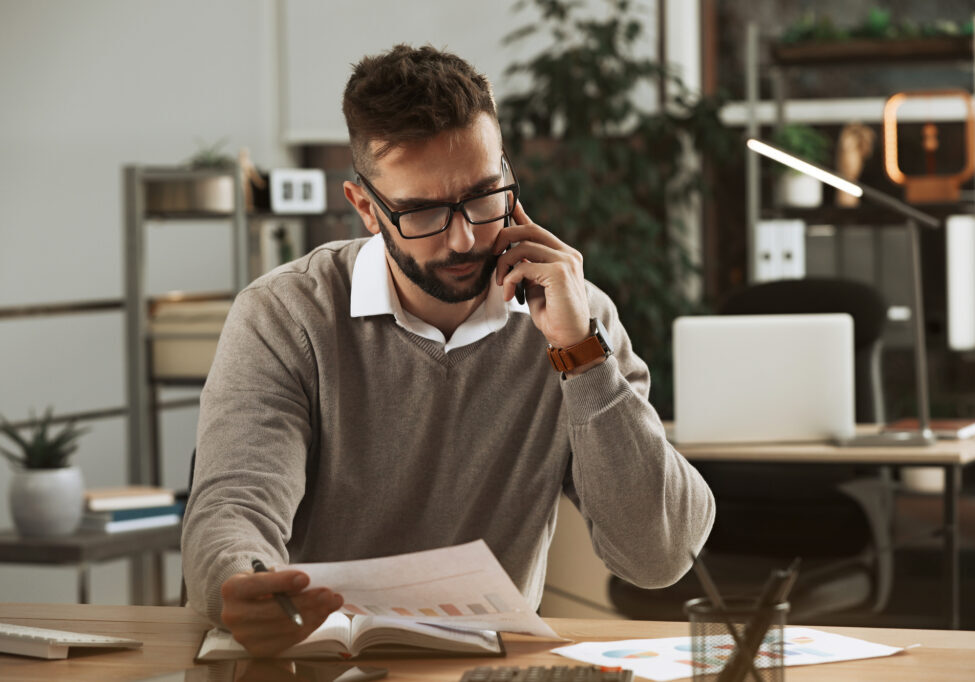 Man talking on phone while working with documents at table in office